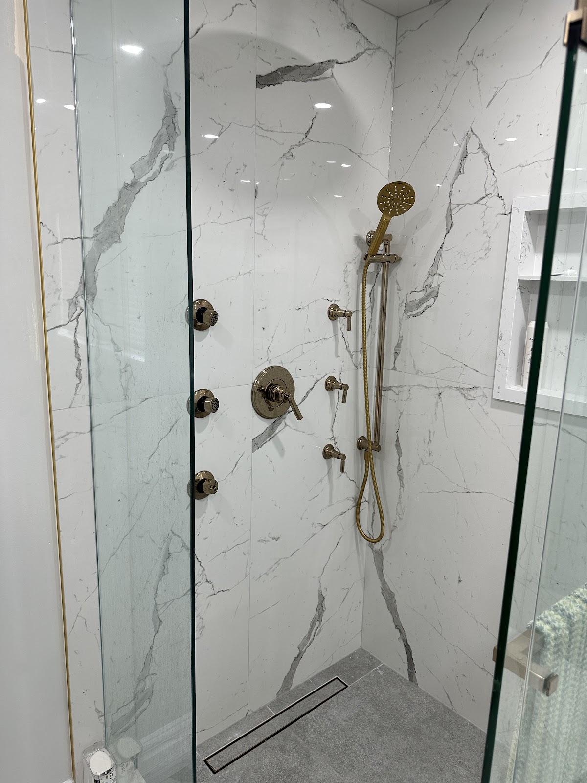 Custom marble-tile shower with brass rainfall fixture and body sprays